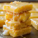 Homemade lemon brownies topped with a zesty lemon glaze on a white plate