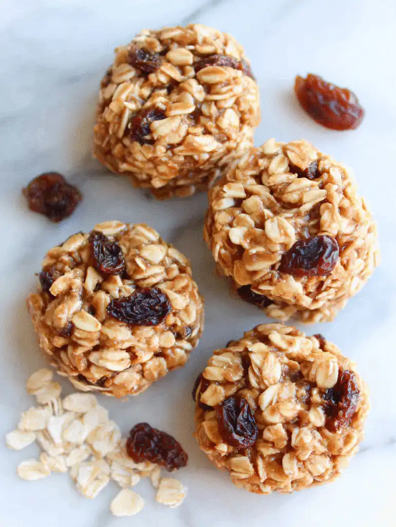 Four no-bake oatmeal desserts : raisin cookies on a marble surface with scattered oats and raisins.