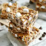 Stacked no bake s’more bars with oatmeal on white marble next to a handwritten recipe card